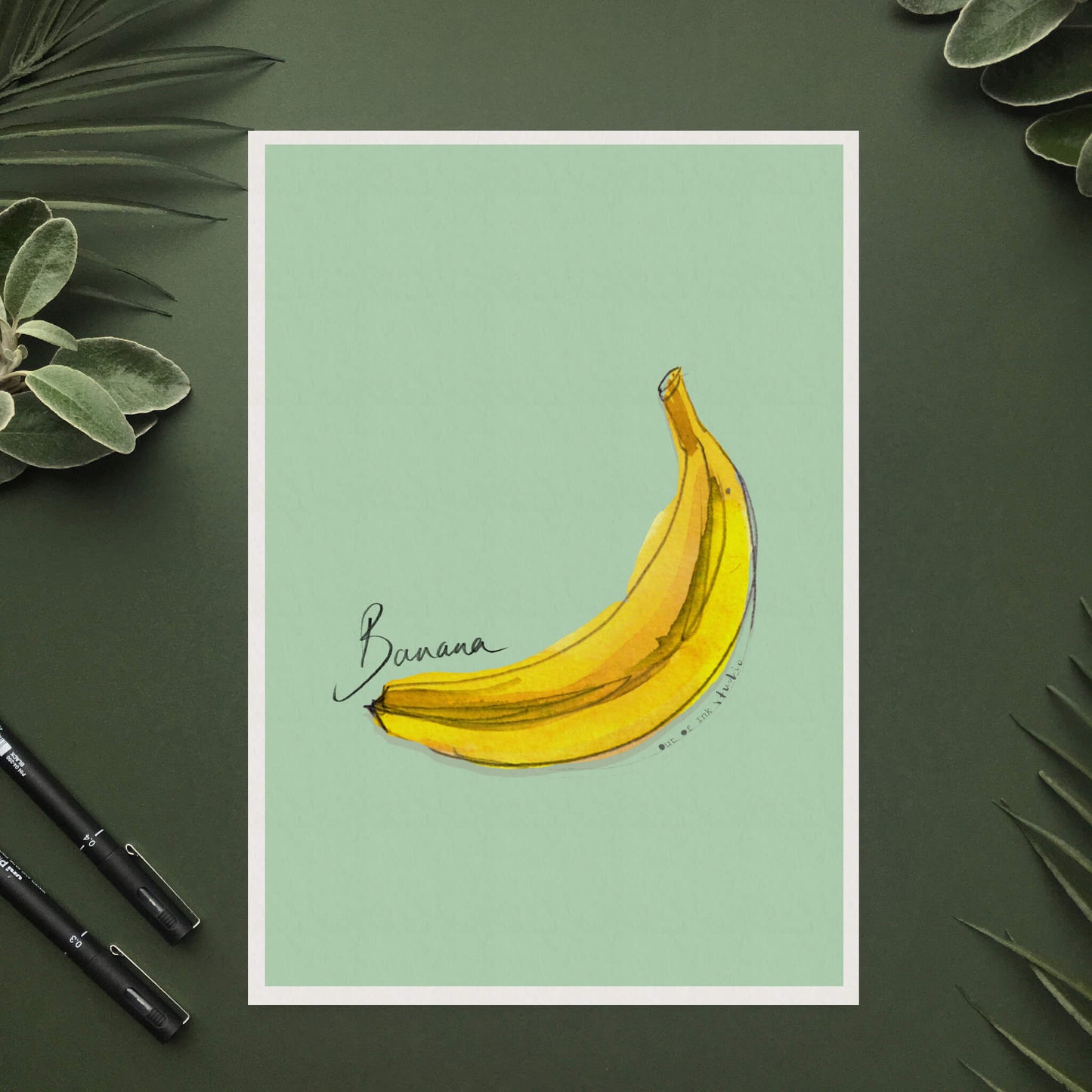 A yellow hand-painted banana on a green background with text ‘banana’ hand written on it.