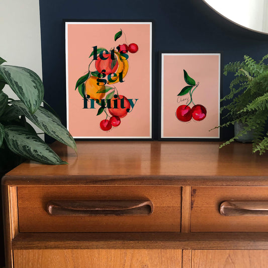 An art print saying Let’s Gift Fruity in text surrounded with hand-painted fruit on a peach background.