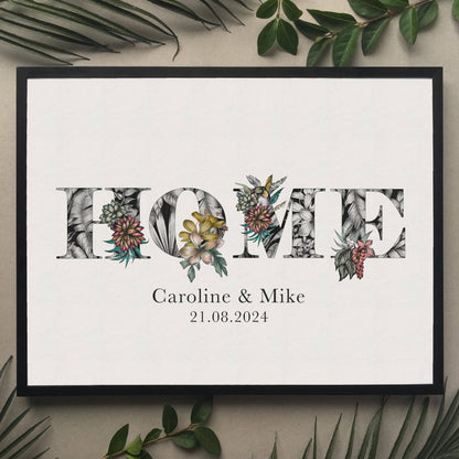 A print of the word 'HOME' filled with tropical imagery. Underneath the print is personalised with couples names  and moving in date. Hung on wall in black frame.