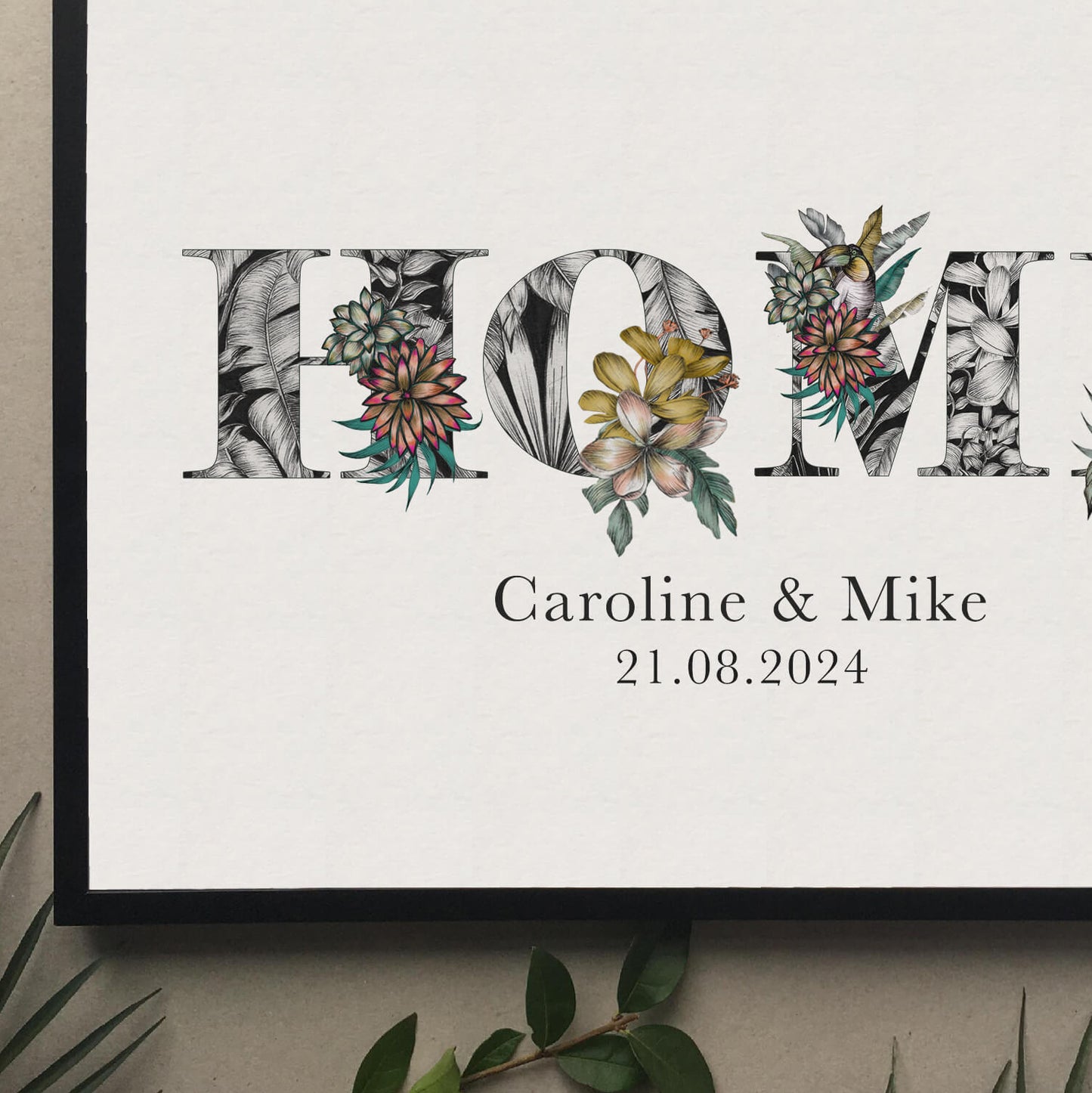 A print of the word 'HOME' filled with tropical imagery. Underneath the print is personalised with couples names and moving in date. Hung on wall in black frame.