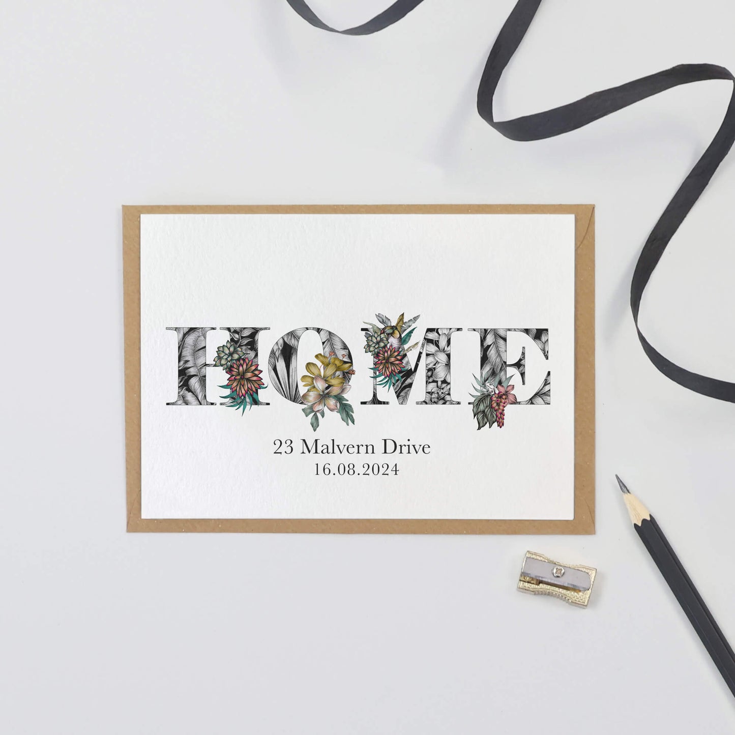 'HOME' printed on a card. Personalised with the first line of their address and moving in date printed underneath.