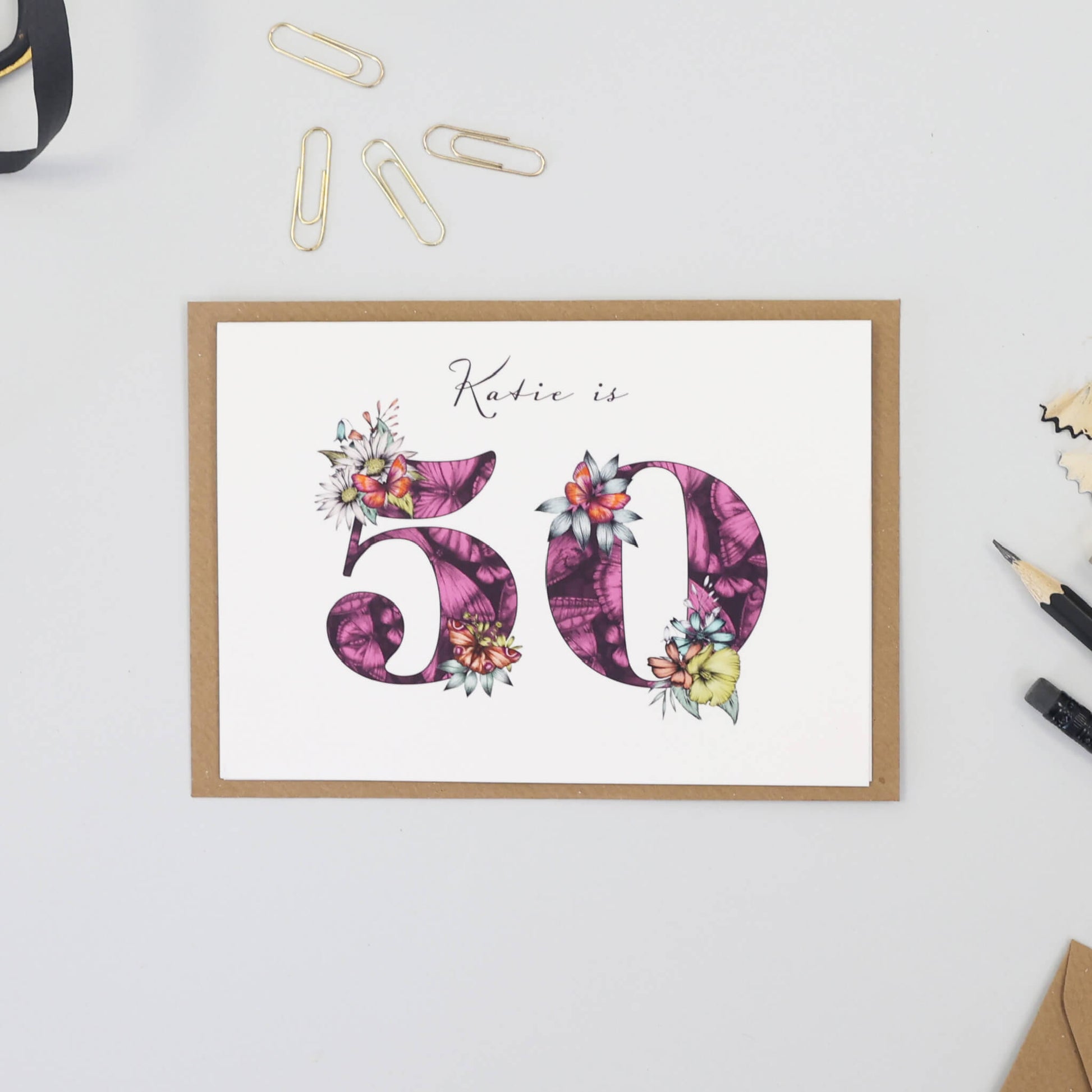 Personalised 50th birthday card with age filled with hand-drawn butterflies and flowers. The recipients name is printed above age.