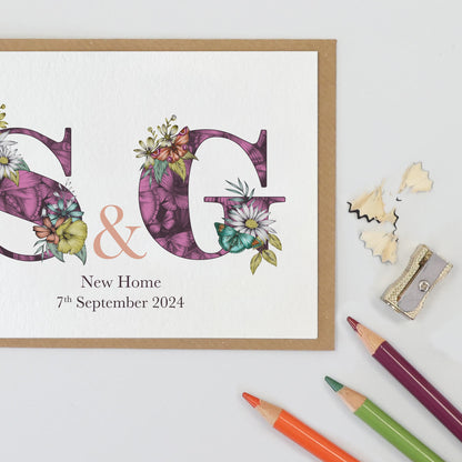 Purple personalised housewarming card with S & g initials filled with hand-drawn butterflies and flowers. The wording ‘New Home and the moving in date is printed underneath initials.