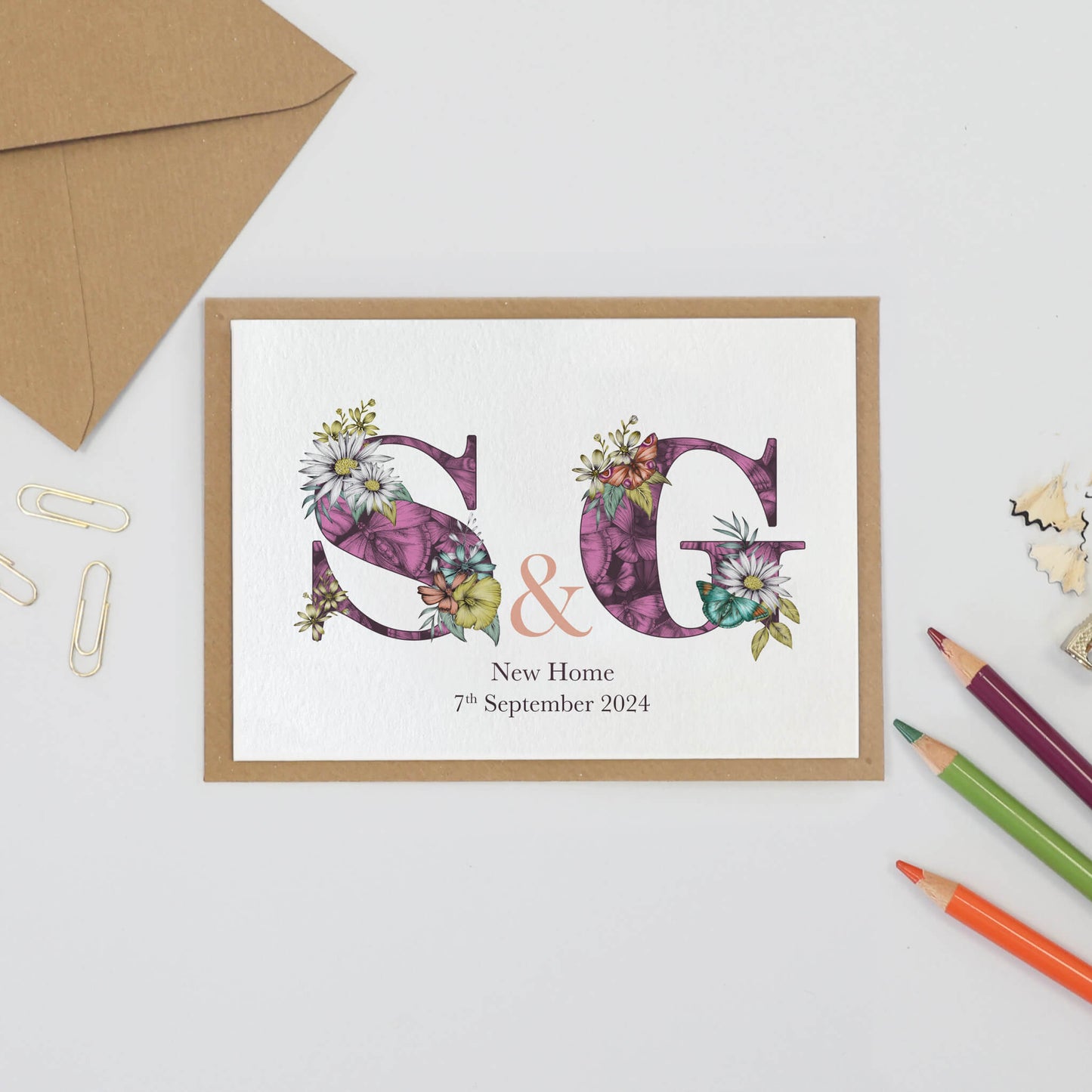 Purple personalised housewarming card with S & g initials filled with hand-drawn butterflies and flowers. The wording ‘New Home and the moving in date is printed underneath initials.